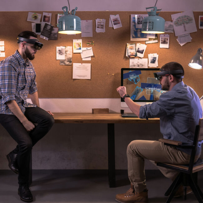 L'Image présente deux personnes portant des casque Hololens en train de travailler ensemble sur de la réalité mixte.