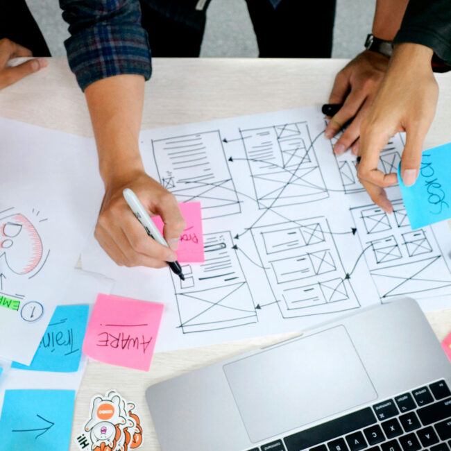 L'image présente plusieurs personnes en train de travailler ensemble sur la maquette papier d'une application.